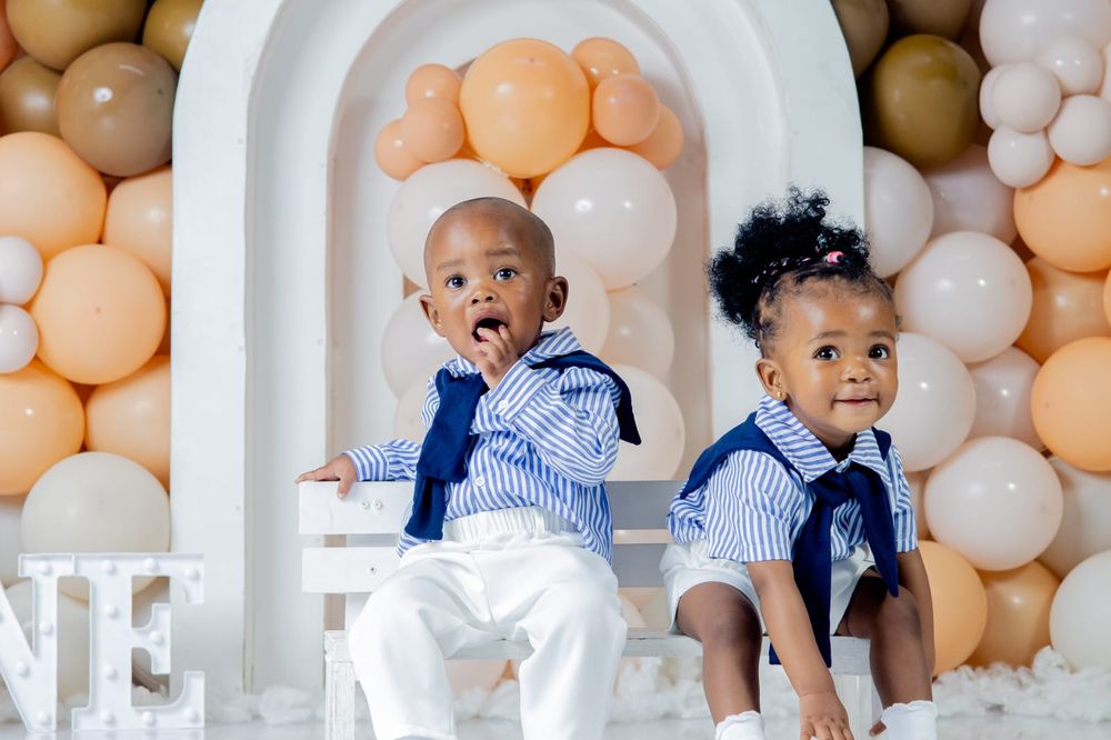 Two babies smiling in front of a balloon backdrop